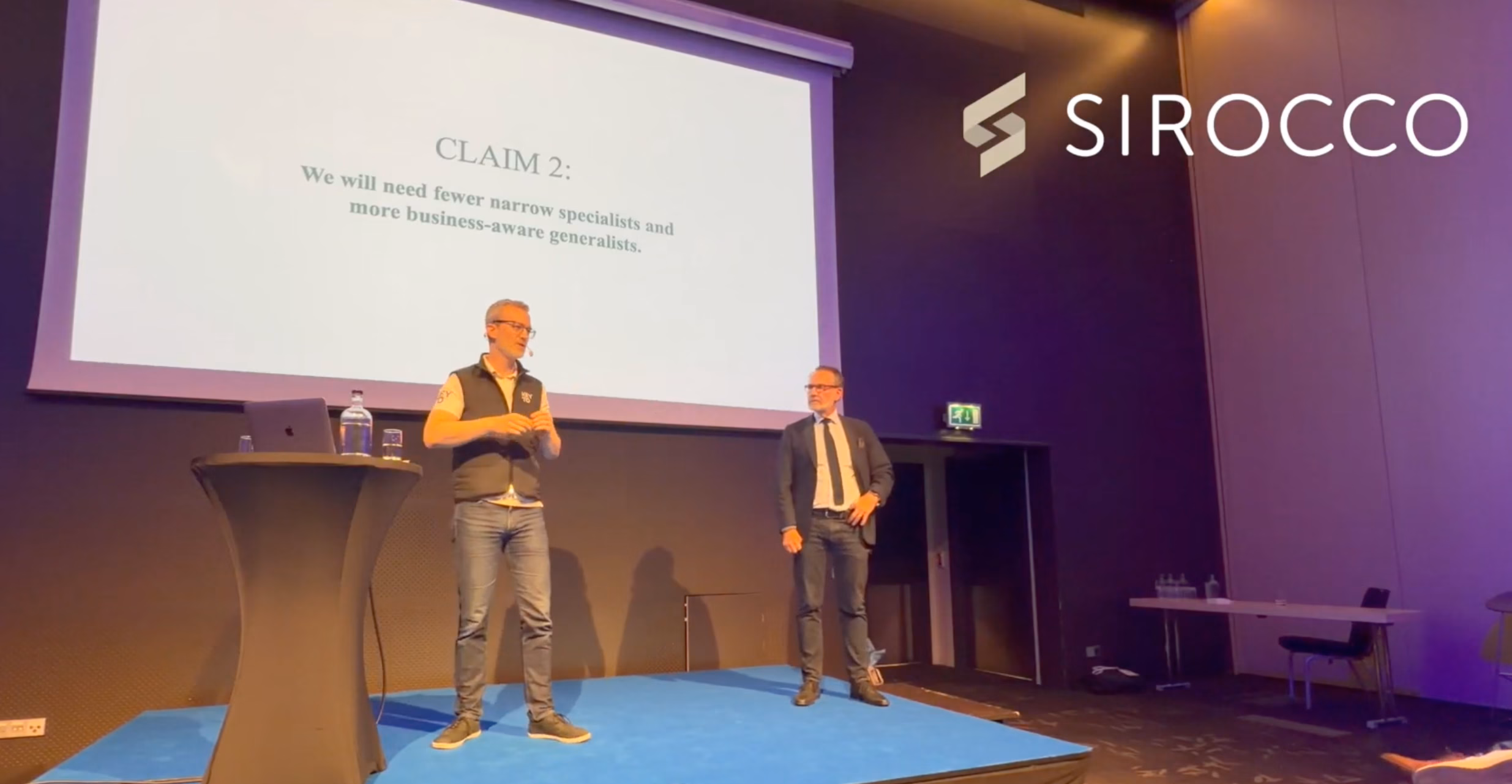 Martin Doktår Wilén and Mats Dahl on stage at the keynote, with the slide reading: Claim 2 - We will need fewer narrow specialists and more business-aware generalists.